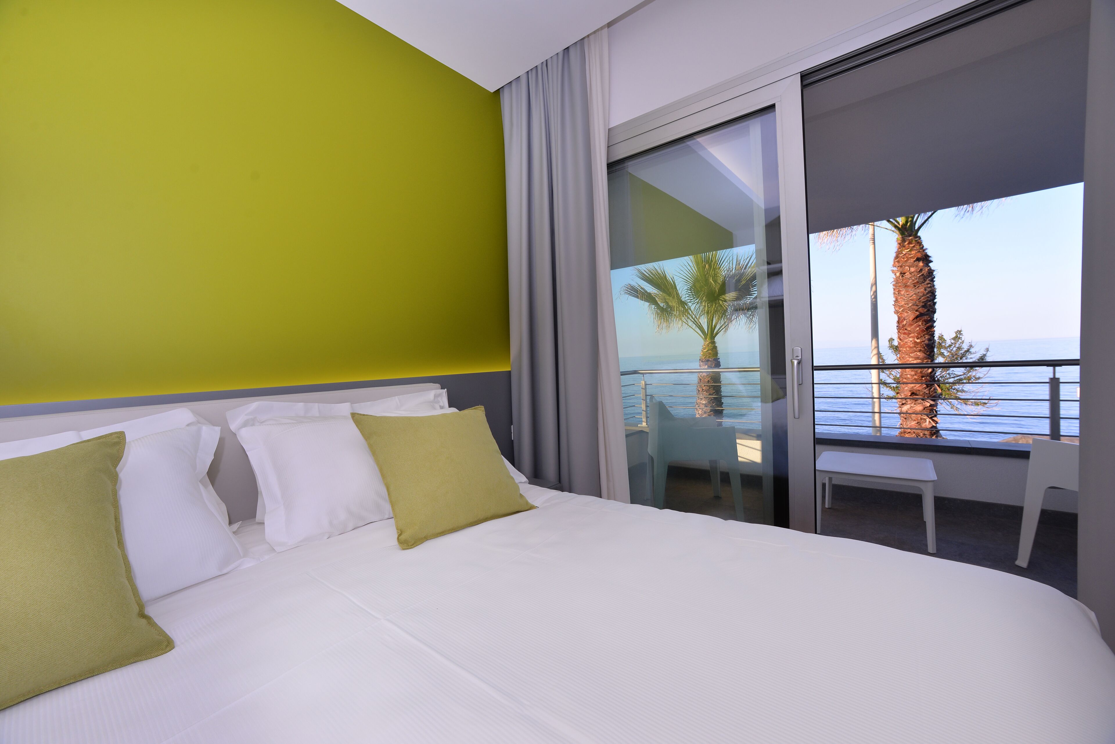 Une chambre d’hôtel avec un lit, un balcon donnant sur la mer et un palmier.