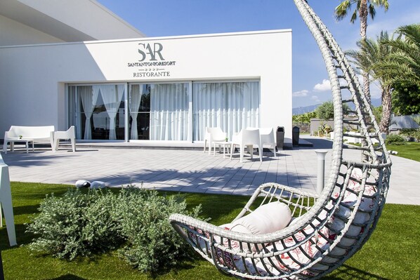 Un moderno resort con fachada blanca, zona de estar al aire libre y una silla colgante.