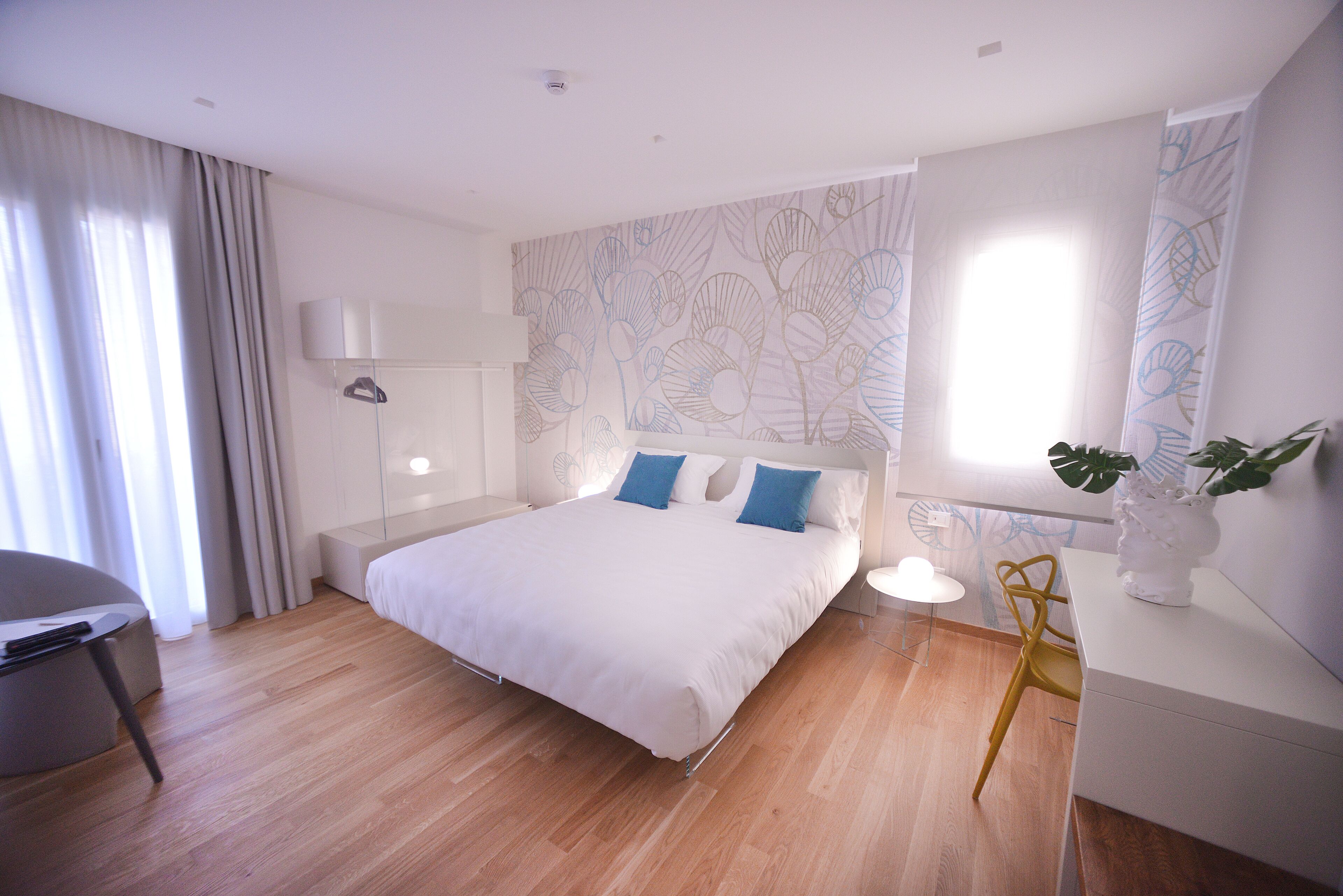 A modern hotel room with a large bed, a desk, a chair, and a window with curtains.