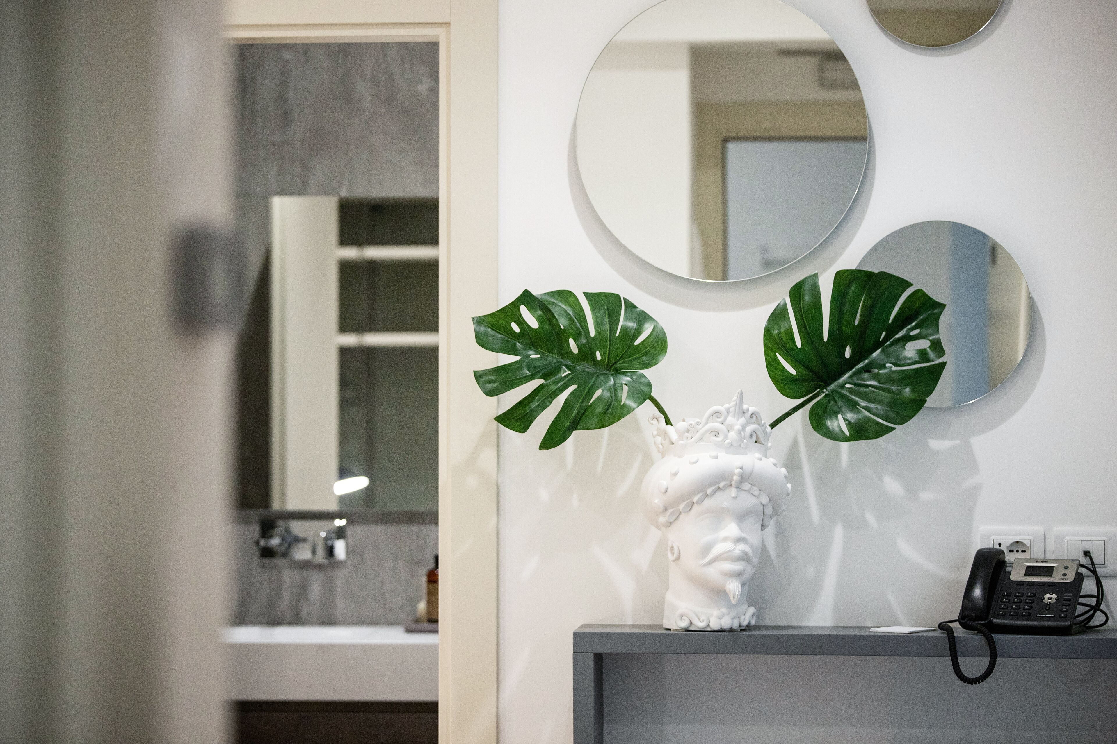 A bathroom with a white vanity, a white bust sculpture, and a telephone.