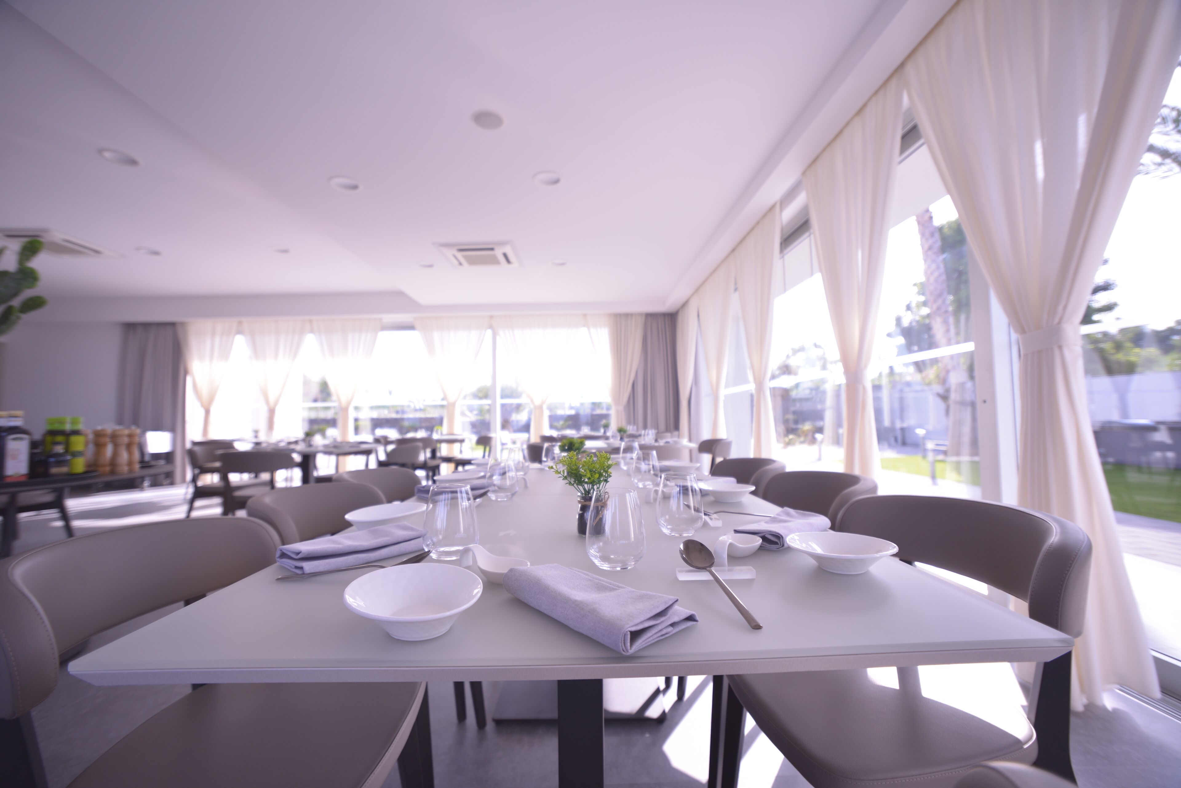 A dining area with tables set for service, large windows, and a view of the outdoors.