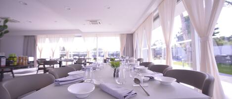 A dining area with tables set for service, large windows, and a view of the outdoors.