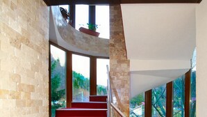 A staircase with red carpet and metal railings, leading to a balcony with potted plants.