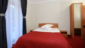 Una habitación de hotel con una cama, una mesita de noche, un armario de madera y una ventana con cortinas negras.