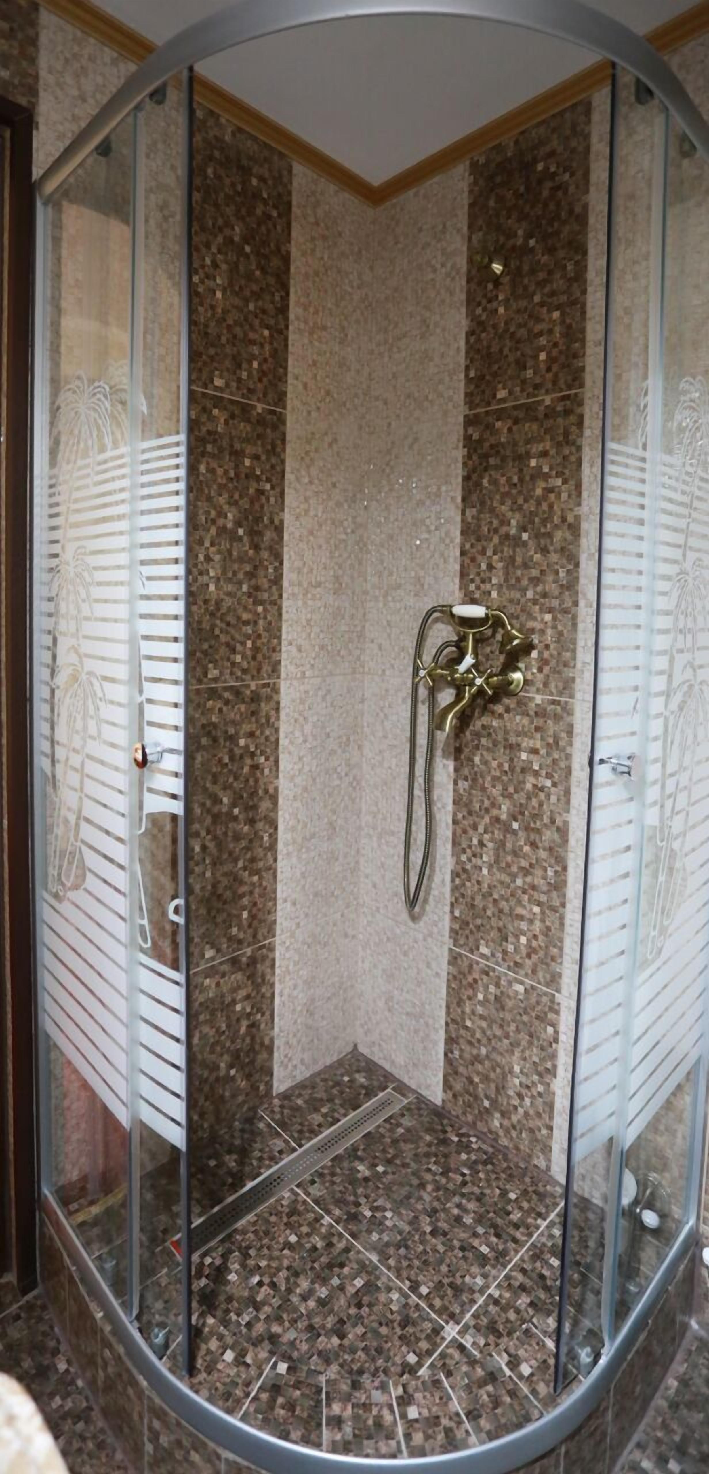 A glass-enclosed shower with a curved design, a showerhead, and a tiled floor.