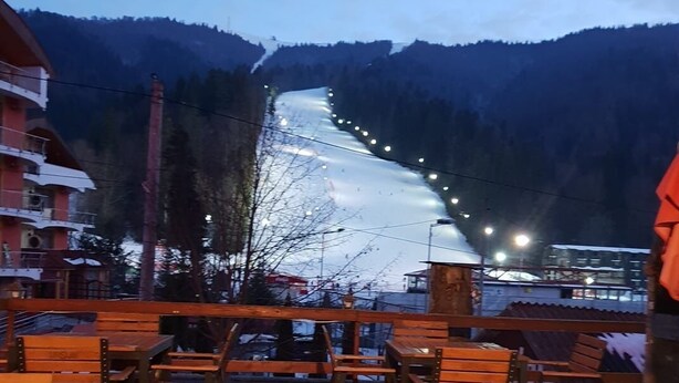 A terrace with wooden tables and chairs overlooking a snow-covered slope with lights.