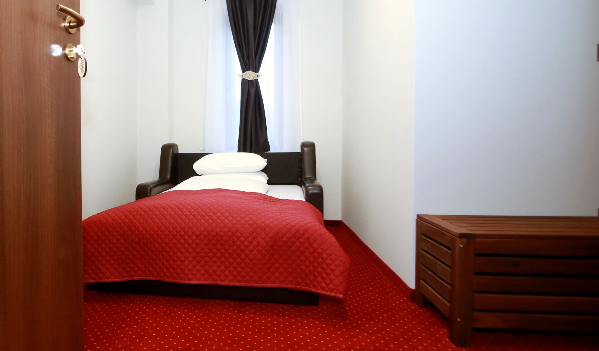 Una habitación de hotel con una cama, un banco de madera y una alfombra roja.
