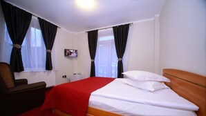 A hotel room with a bed, a chair, a TV, and a window with curtains.