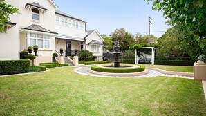 Un jardin bien entretenu, agrémenté d’une fontaine centrale, de haies taillées avec soin et d’un belvédère blanc.