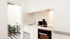 A compact kitchen with white cabinetry, a built-in oven, a dishwasher, and a coffee maker.