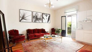 A living room with a red sofa set, a coffee table with books, and a large window with a view. - Beautiful Studio in Heritage Building with Balcony (Lewsiham)