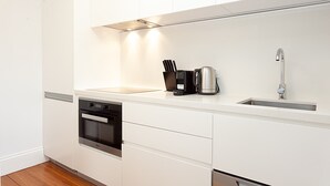 A modern kitchen with white cabinetry, a built-in oven, a stainless steel kettle, and a sink with a faucet. - Beautiful Studio in Heritage Building with Balcony (Lewsiham)
