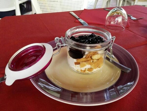 A dessert in a glass jar with a metal clasp lid, placed on a saucer on a table with a red tablecloth. - Albergo Il Sicomoro (Fivizzano)