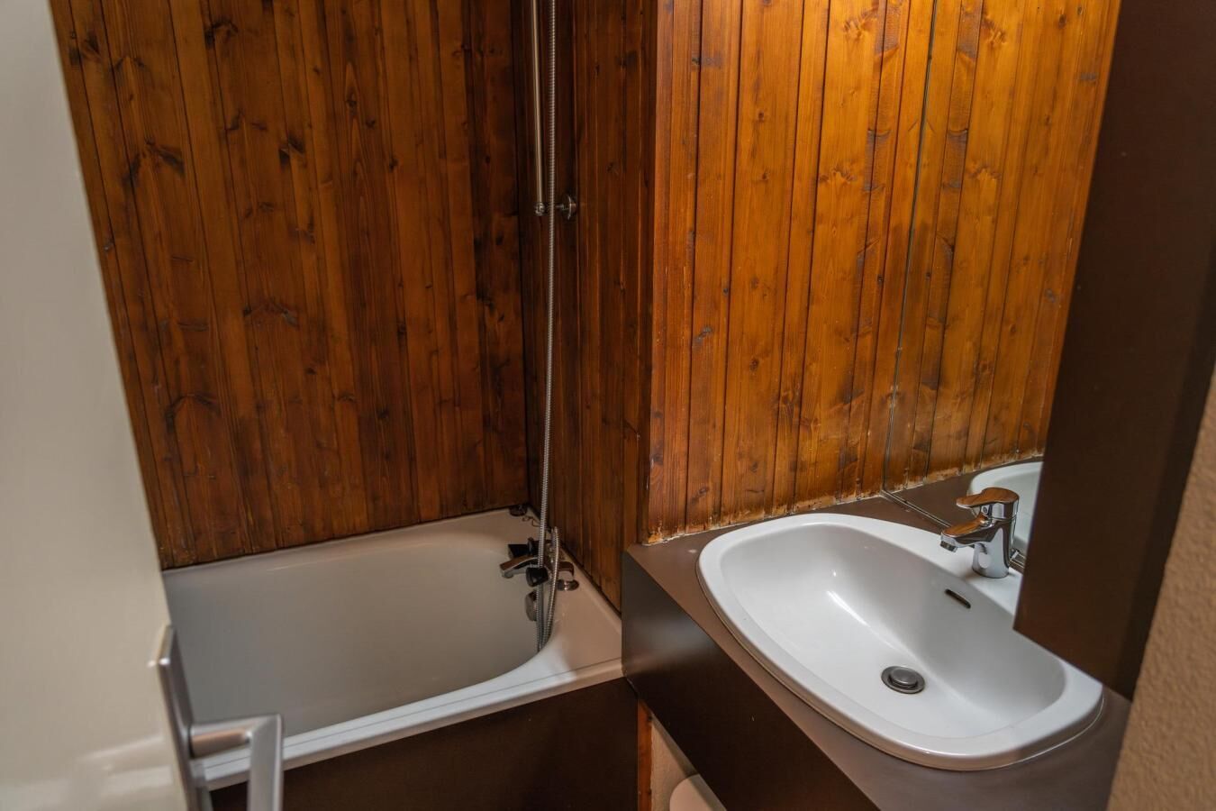 A bathroom with wooden walls, a bathtub, and a sink.