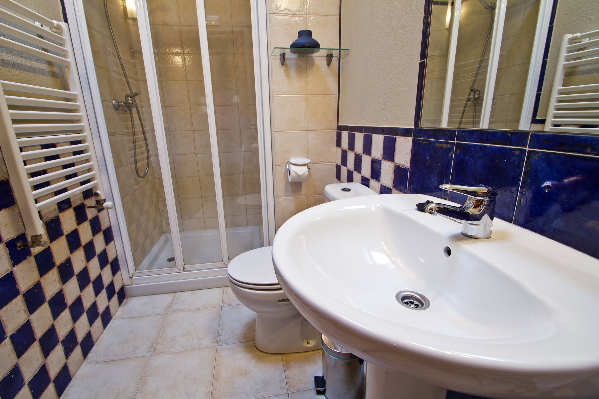 Un baño con cabina de ducha de vidrio, inodoro y lavamanos blancos, y grifo de cromo.