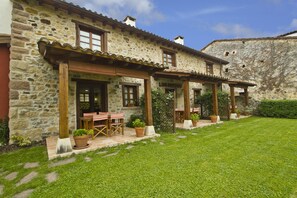 A stone building with a patio area featuring outdoor seating and potted plants. - Apartamentos los Brezos (Anievas)