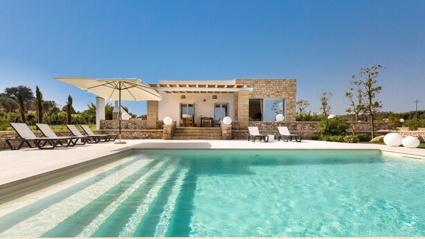 Un área de piscina con sillones de descanso y una pérgola.
