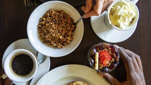 Una mesa de desayuno con diferentes platos, incluyendo tortitas, un frutero y una taza de café.