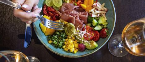 A bowl of mixed fruits and vegetables with a fork, and two glasses of wine on a table.