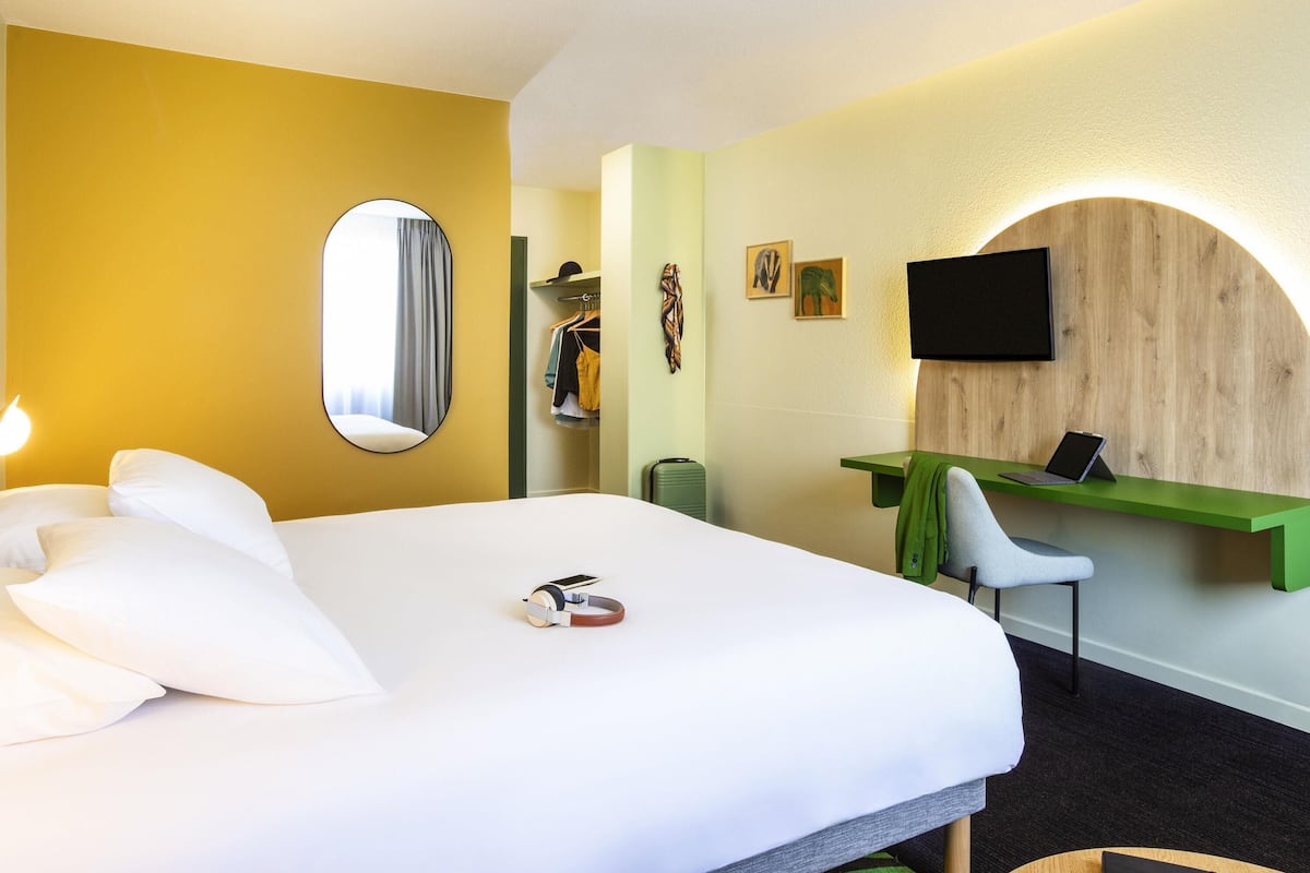 A hotel room with a bed, a desk, a chair, a TV, and a mirror.