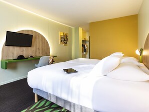 A hotel room with a bed, a desk, a TV mounted on the wall, and a mirror.