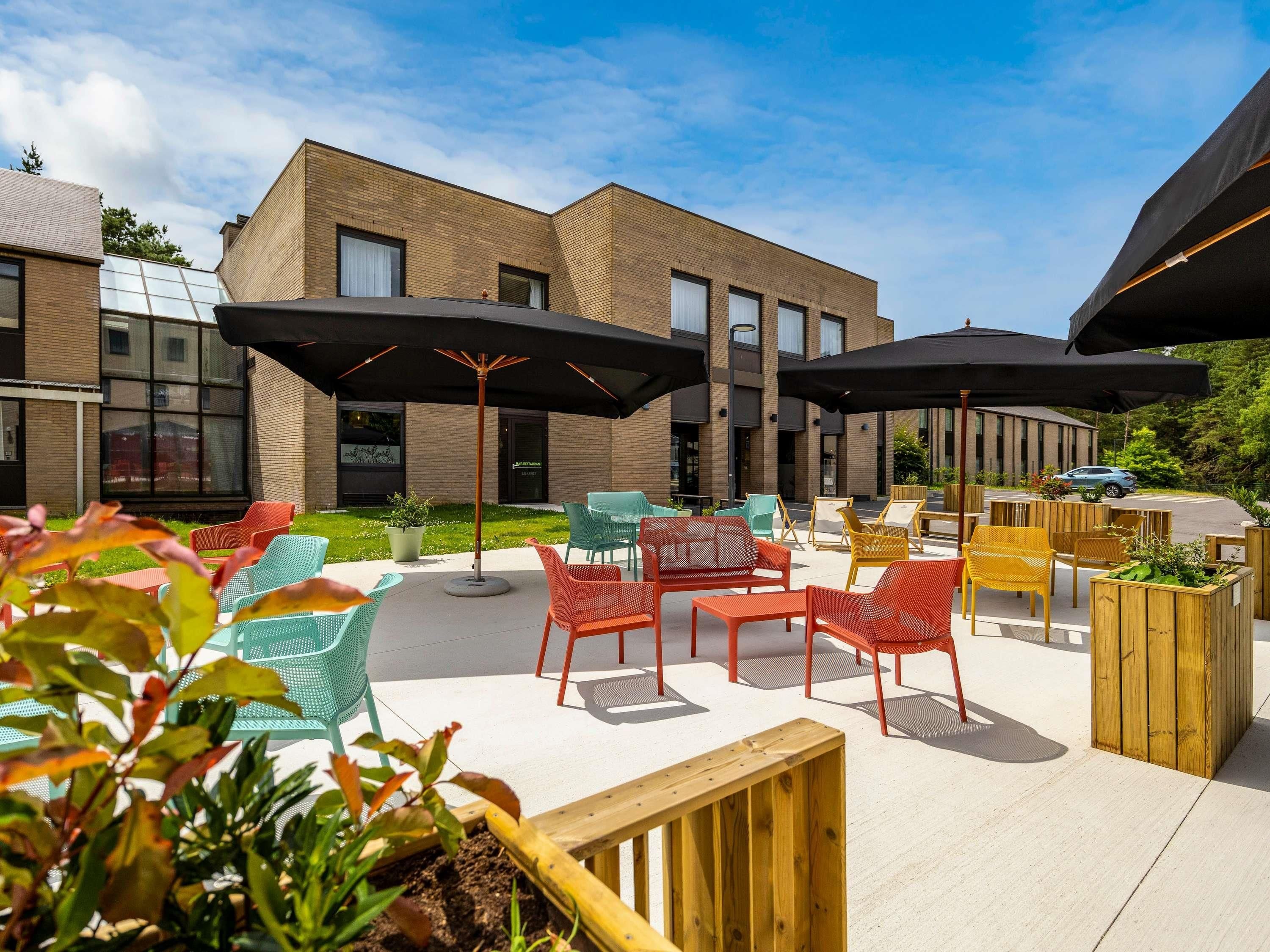 Een terras met verschillende stoelen en tafels, parasols, en een gebouw op de achtergrond.