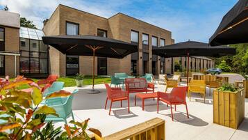 Een terras met verschillende stoelen en tafels, parasols, en een gebouw op de achtergrond.