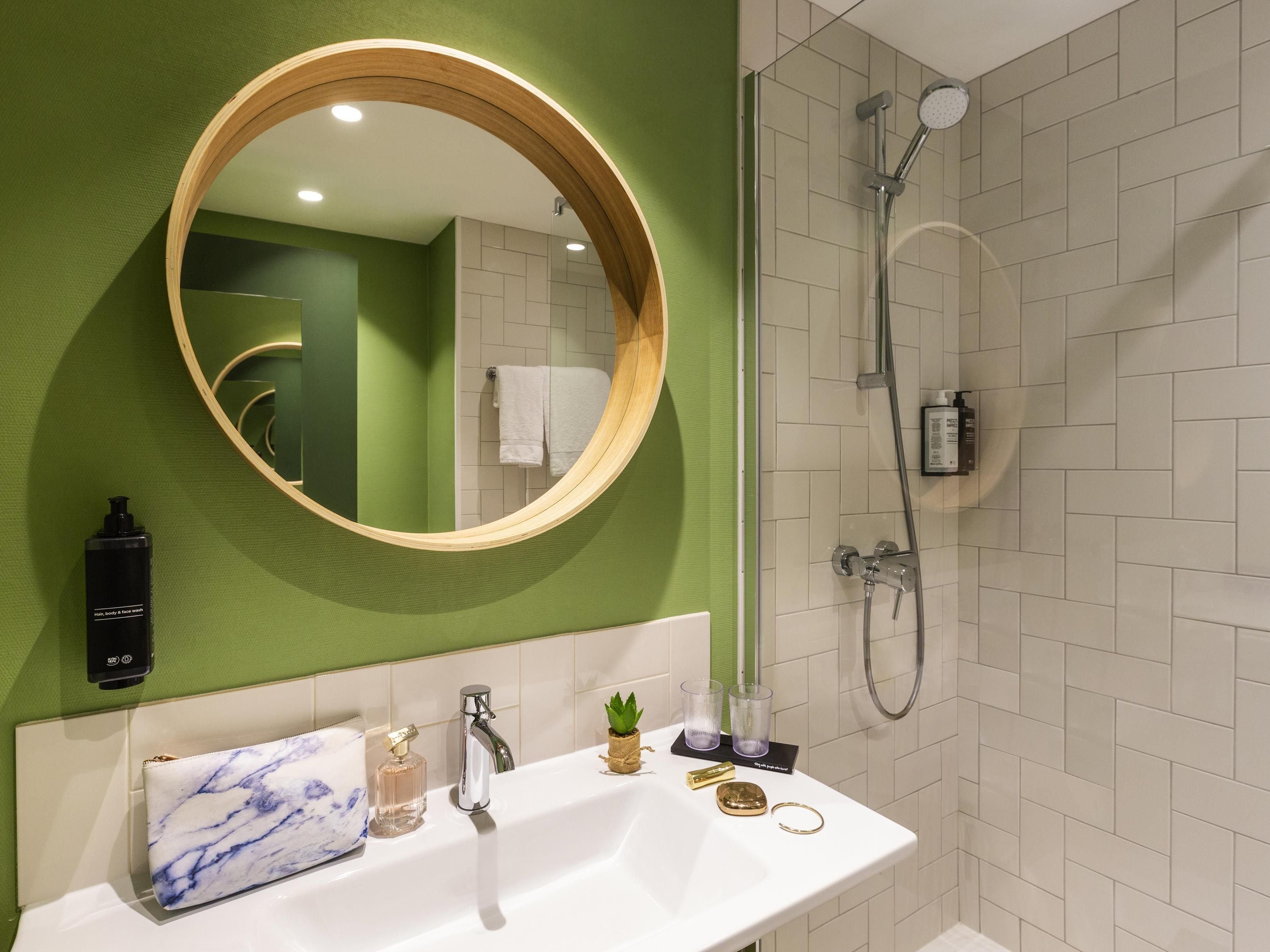 Een moderne badkamer met een ronde spiegel, een witte wasbak en een douche.