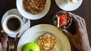 Desayuno con tortitas, una manzana, un muffin, un vaso de jugo, un tazón de granola y una taza de café.