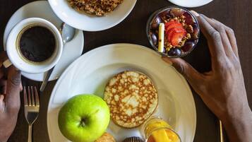 A breakfast setting with pancakes, an apple, a muffin, a glass of juice, a bowl of granola, and a cup of coffee.