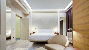 A modern hotel room with a large bed, a seating area with a chair and ottoman, a small table, and a wooden accent wall. - DoubleTree by Hilton Adana (Adana)