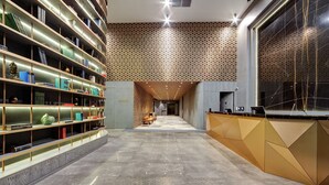 A modern hotel lobby with a central reception desk, a long hallway with bookshelves, and patterned wall designs. - DoubleTree by Hilton Adana (Adana)