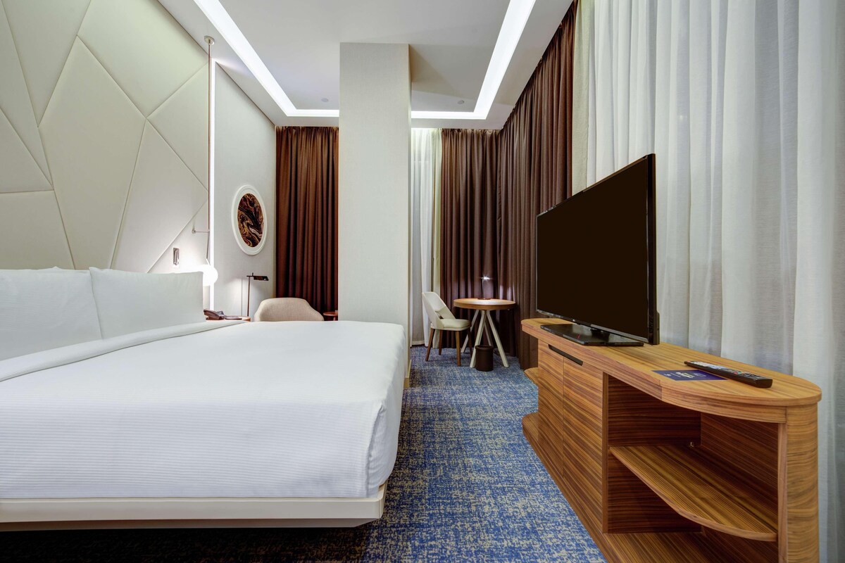 Ein Hotelzimmer mit einem großen Bett, einem Holz-Fernsehschrank, einem Schreibtisch und einem Sessel.