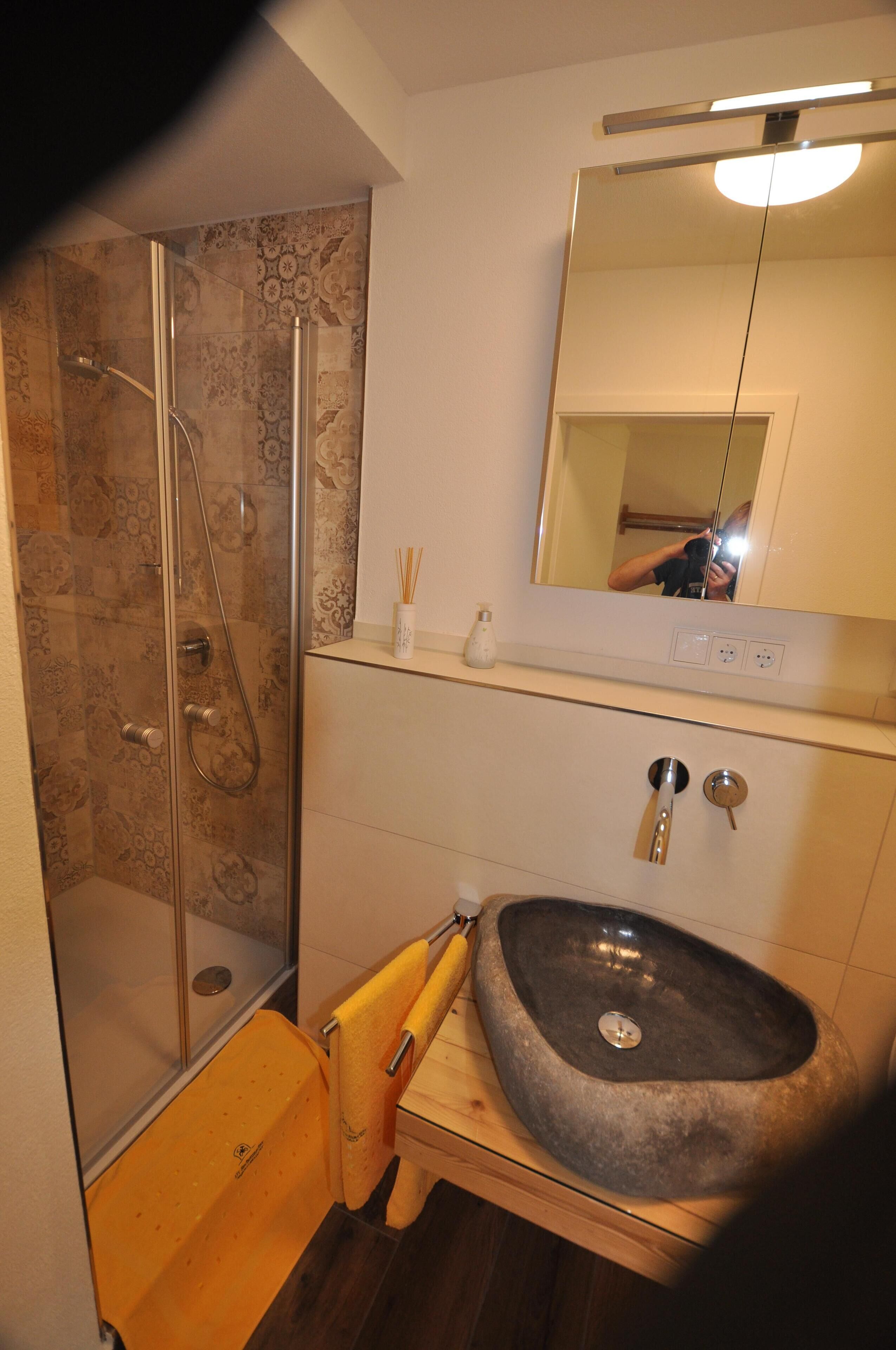 A bathroom with a glass-enclosed shower, a stone sink, and a mirror above the sink.