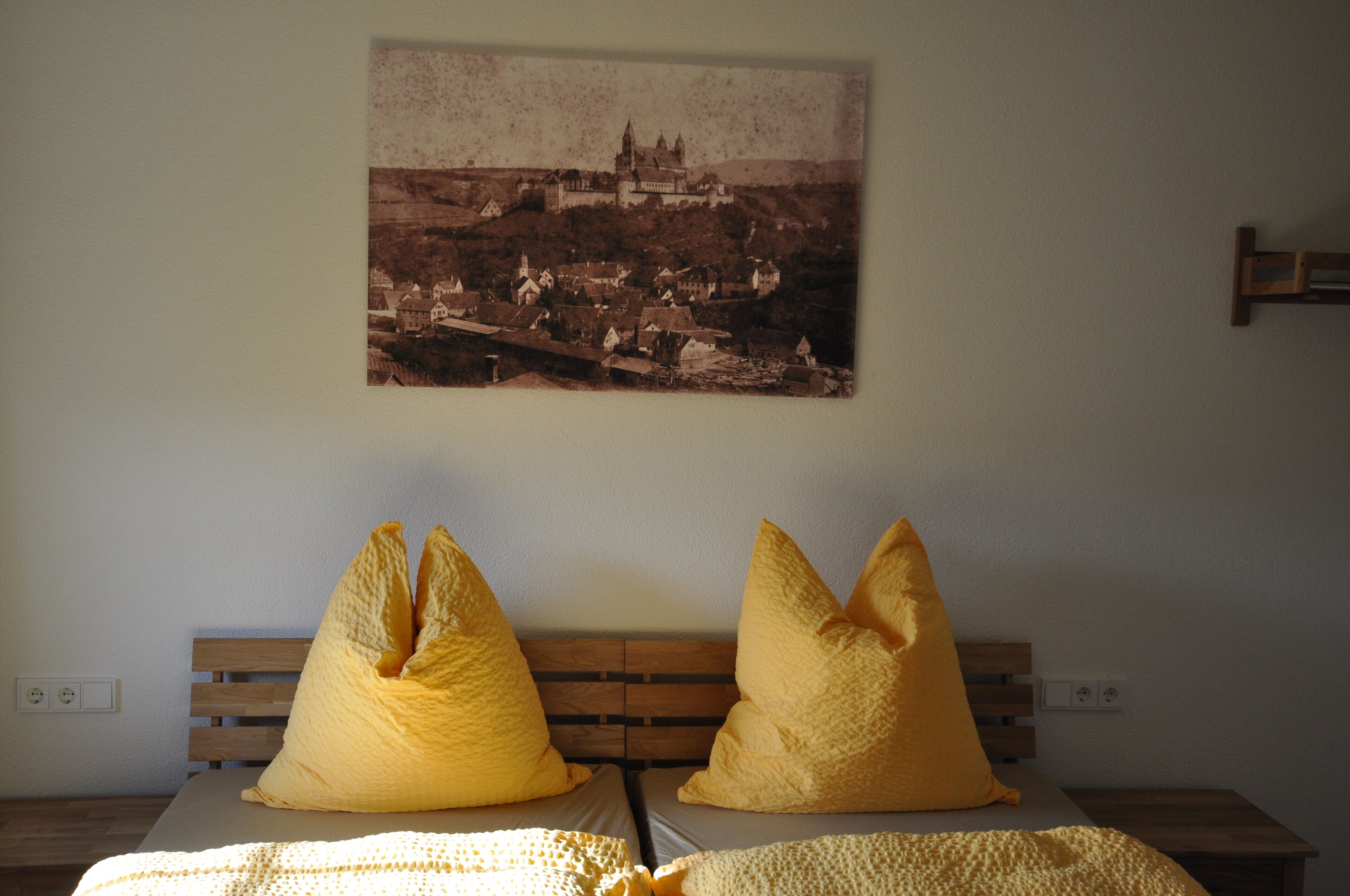 A bedroom with a wooden headboard, a bed with yellow pillows, and a vintage photograph on the wall.