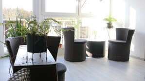 A sunlit patio with wicker furniture, potted plants, and a view of a wooden deck and trees. - D´r Rechenmacher Pension und Landgasthof (Michelfeld)