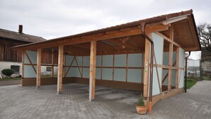 A wooden structure with a sloped roof, possibly a covered area or shed, with a brick-paved ground. - D´r Rechenmacher Pension und Landgasthof (Michelfeld)