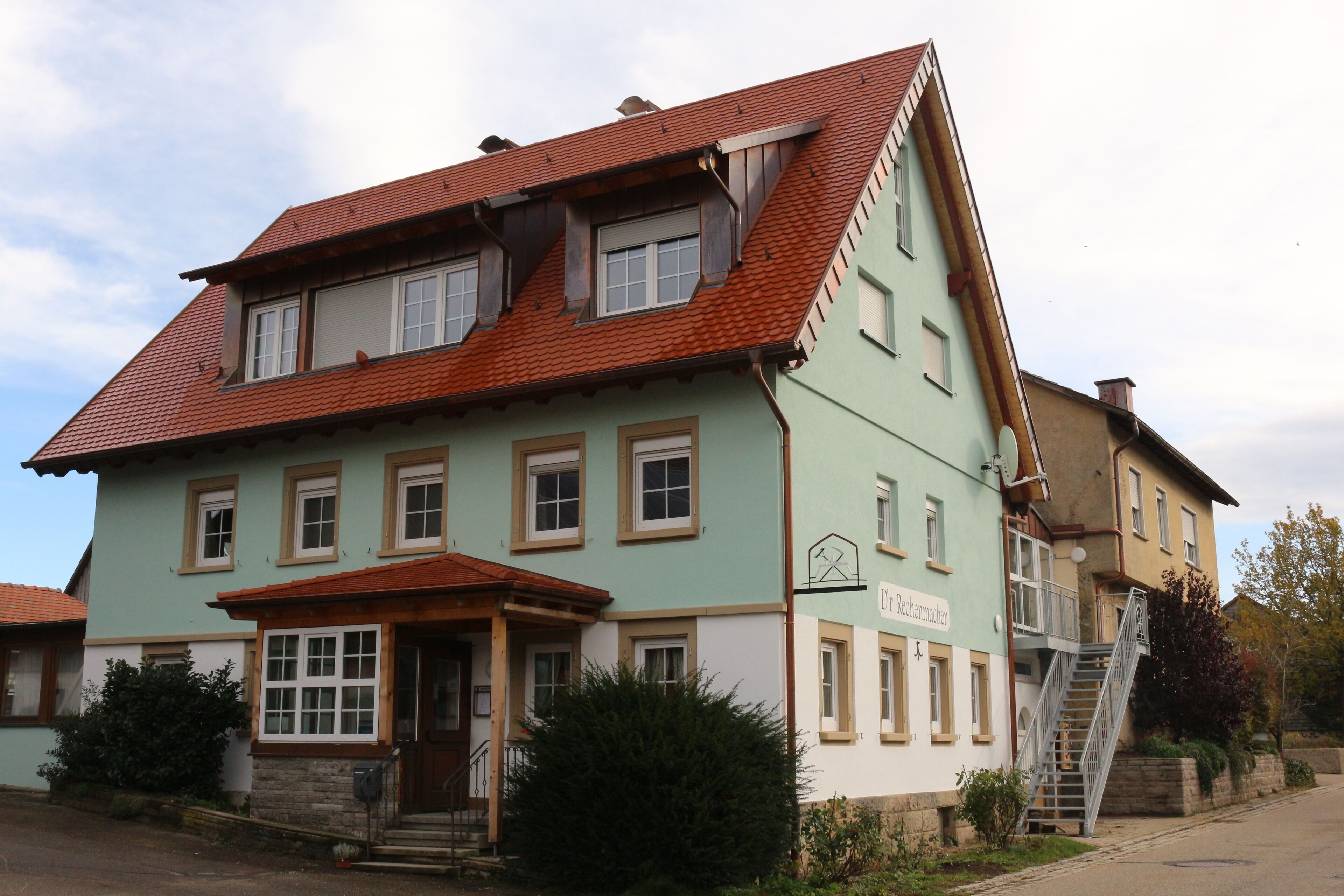 A two-story building with a steeply pitched red-tiled roof, multiple windows, and a visible staircase leading to an upper floor.