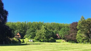 Een landelijk landschap met een helderblauwe lucht, een omheind veld en twee houten hutten met rode daken.