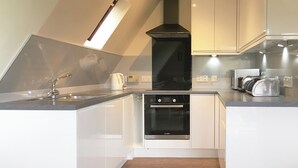 Een moderne keuken met witte kasten, een Bosch oven, een zwarte afzuigkap en een houten vloer.