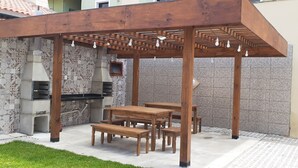 Eine Terrassengaststätte mit Holztischen und -bänken, einer Pergola mit hängenden Lichtern sowie einer Steinwand mit integriertem Grill.