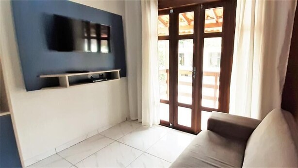 Ein Wohnzimmer mit Flachbildfernseher an der Wand, einer Couch und einer Glasschiebetür zu einem Außenbereich.