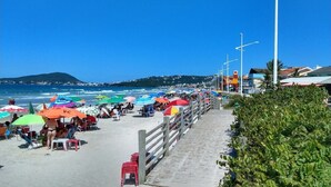 Ein Strand mit bunten Sonnenschirmen, einer Holzpromenade und Blick auf das Meer sowie hügelige Fernlandschaft.
