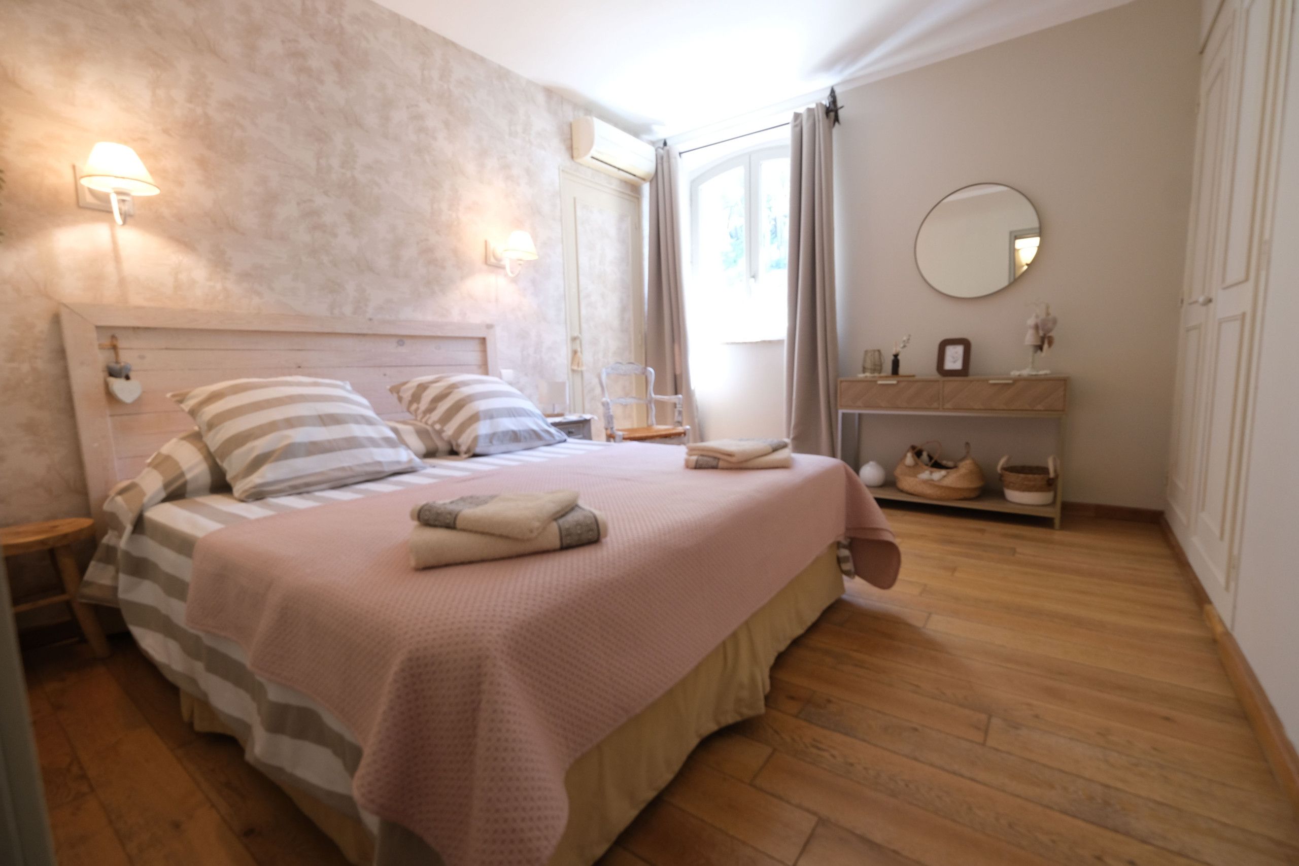 Un dormitorio con cama, mesitas de noche, cómoda, espejo y ventana con cortinas.