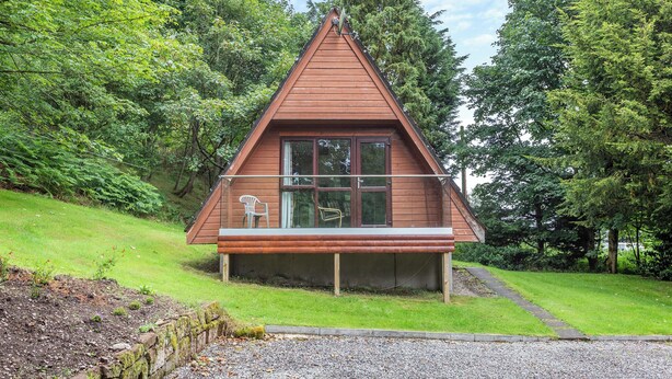 A wooden cabin with a triangular roof, a balcony, and a window. - Gorse Lodge - UK7050 (Rosemarkie, near Fortrose)