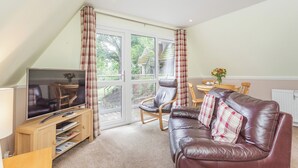 A cozy living room with a brown leather sofa, a wooden TV stand, and a dining area with a table and chairs. - Gorse Lodge - UK7050 (Rosemarkie, near Fortrose)