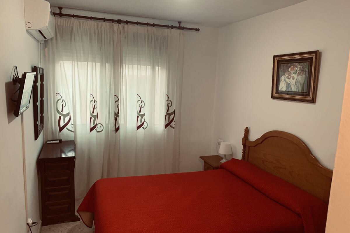 Une chambre à coucher avec un lit, une tête de lit en bois, une table de chevet avec une lampe, un miroir, un climatiseur et un tableau encadré accroché au mur.