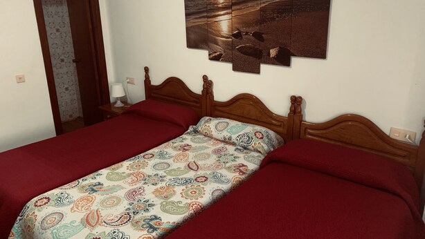 Ein Schlafzimmer mit einem hölzernen Bett, einer gemusterten Tagesdecke und einem Wandbild, das eine Strandansicht zeigt.