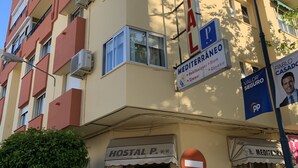 Ein mehrgeschossiges Gebäude mit einem Schild, auf dem 'Hostal P.' und 'Mediterraneo' stehen, was auf eine Jugendherberge und ein Restaurant hindeutet.