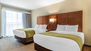 A hotel room with two beds, a large window with curtains, a wall-mounted light fixture, and a carpeted floor.
